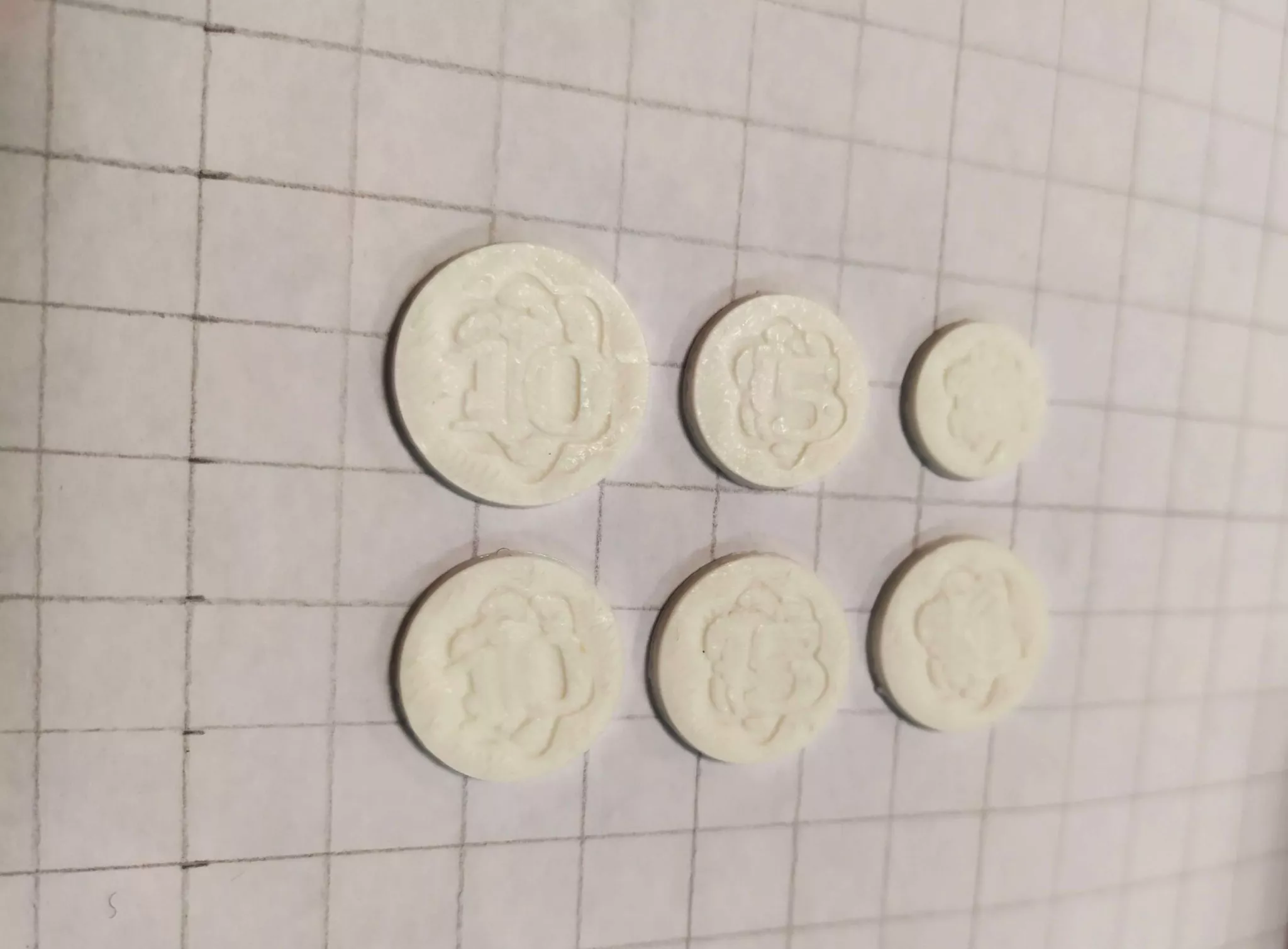 Des pièces de "monnaie" en plastique imprimées en 3D. Les détails sont indistincts mais on devine un motif et les chiffres "10" et "5".